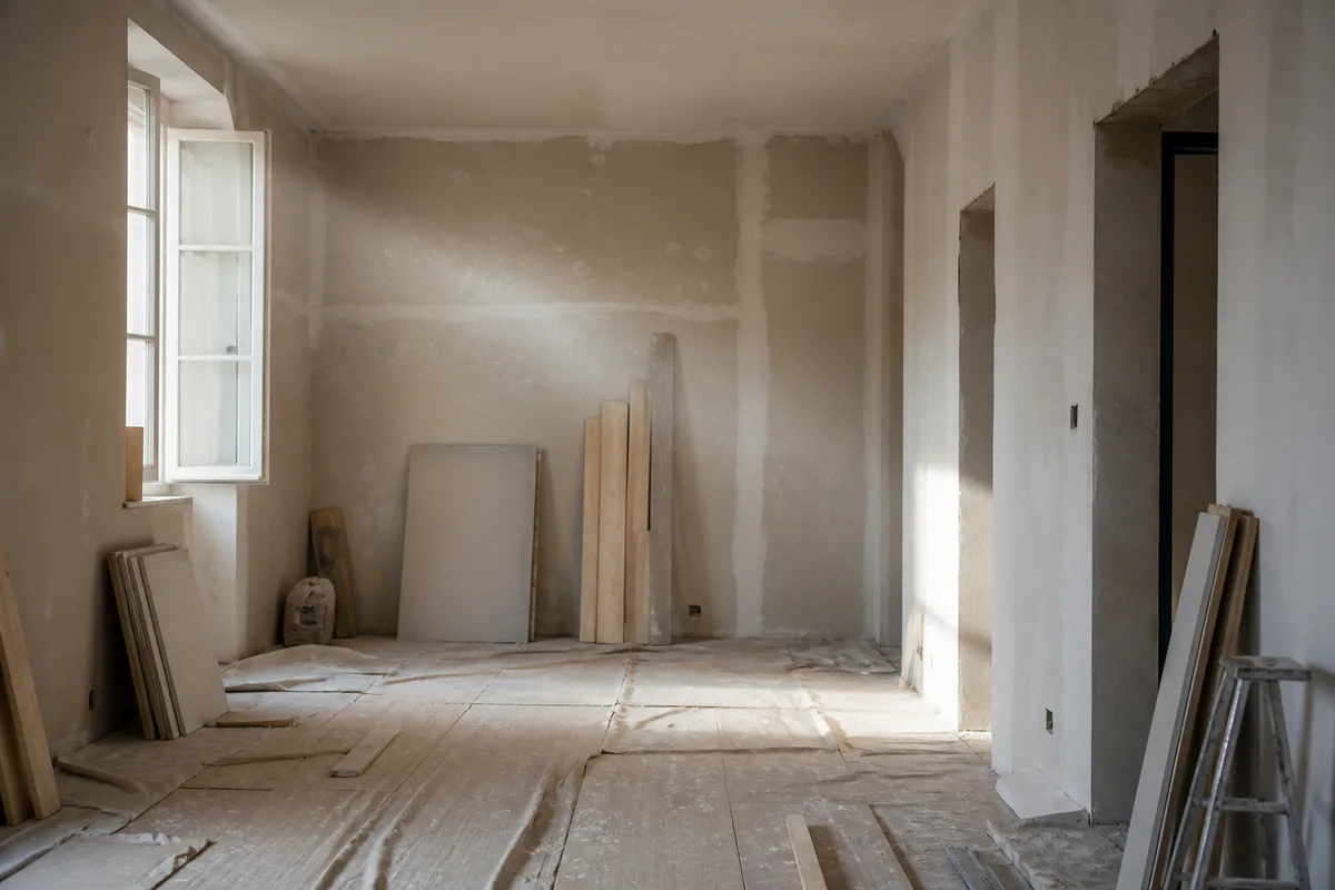 Pièce en cours de rénovation avec sol protégé, murs décapés et matériaux stockés